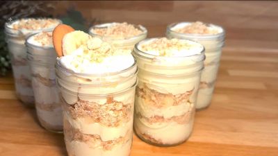 Banana pudding parfaits with whipped cream and crushed cookies in mason jars on a wooden table.
