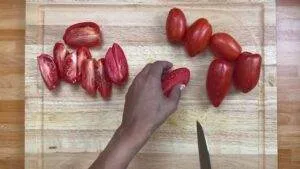 Hand slicing fresh Roma tomatoes on a wooden cutting board, perfect for cooking or salads.