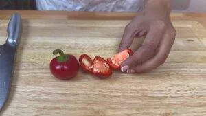 Person slicing red peppers on a wooden cutting board with a knife nearby.