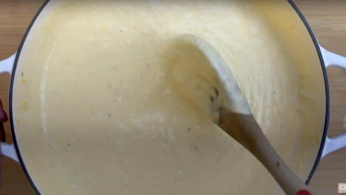 Creamy cheese sauce being stirred with a wooden spoon in a white pot.
