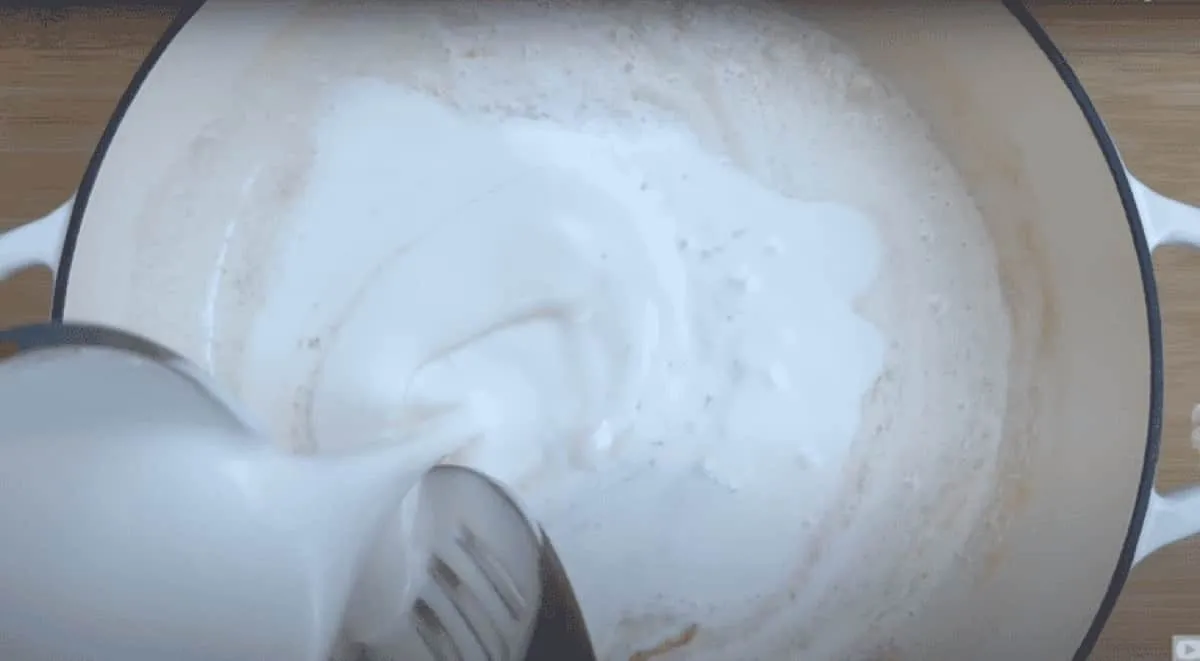 Pouring creamy liquid into a pot for cooking, blending smooth ingredients.