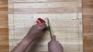 Slicing fresh red and green chili peppers on a wooden cutting board for a spicy recipe preparation.