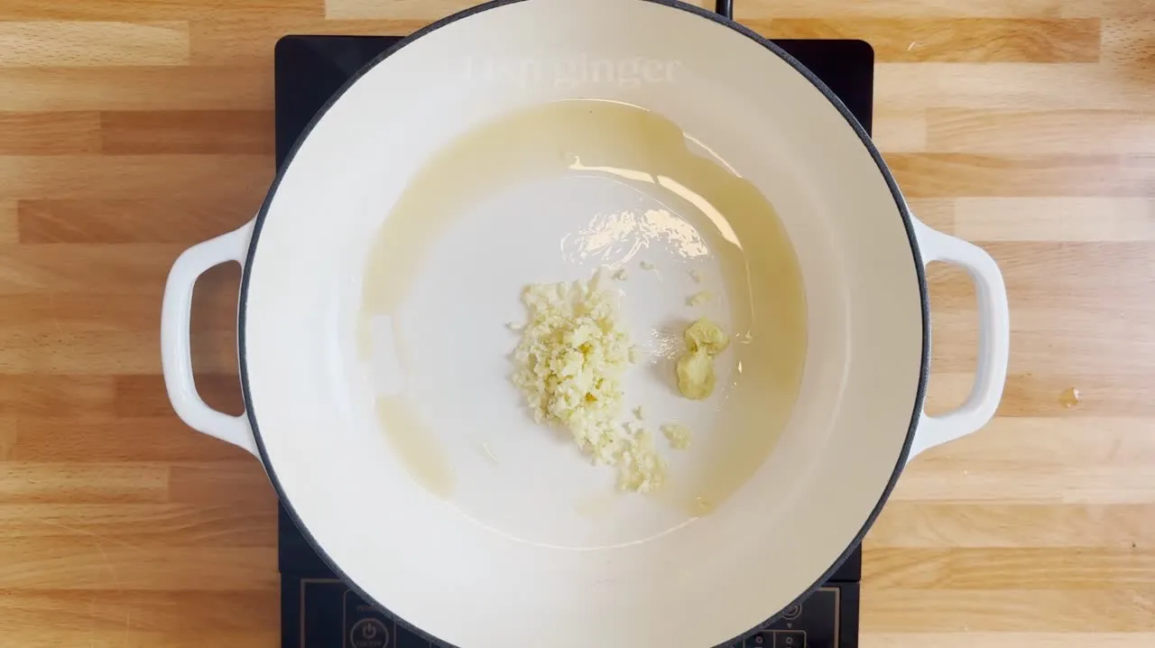 Chopped garlic in oil in a white pot on a wooden surface, ready for cooking.