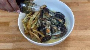 Mussels in creamy sauce with crispy fries in a bowl, finished with a drizzle of olive oil.