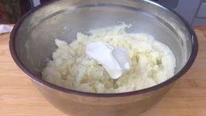 Bowl of creamy mashed potatoes with a dollop of sour cream, ready for mixing on a wooden countertop.