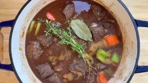 Hearty beef stew with carrots, celery, bay leaf, and thyme in a Dutch oven. Perfect comforting and savory meal.