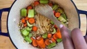 Person stirring chopped carrots, celery, and onions in a pot with a wooden spoon. Perfect for a homemade soup recipe.