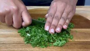 Person chopping fresh parsley on a wooden cutting board.