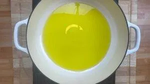 Overhead view of a white pot with hot olive oil on a wooden surface, ready for cooking.