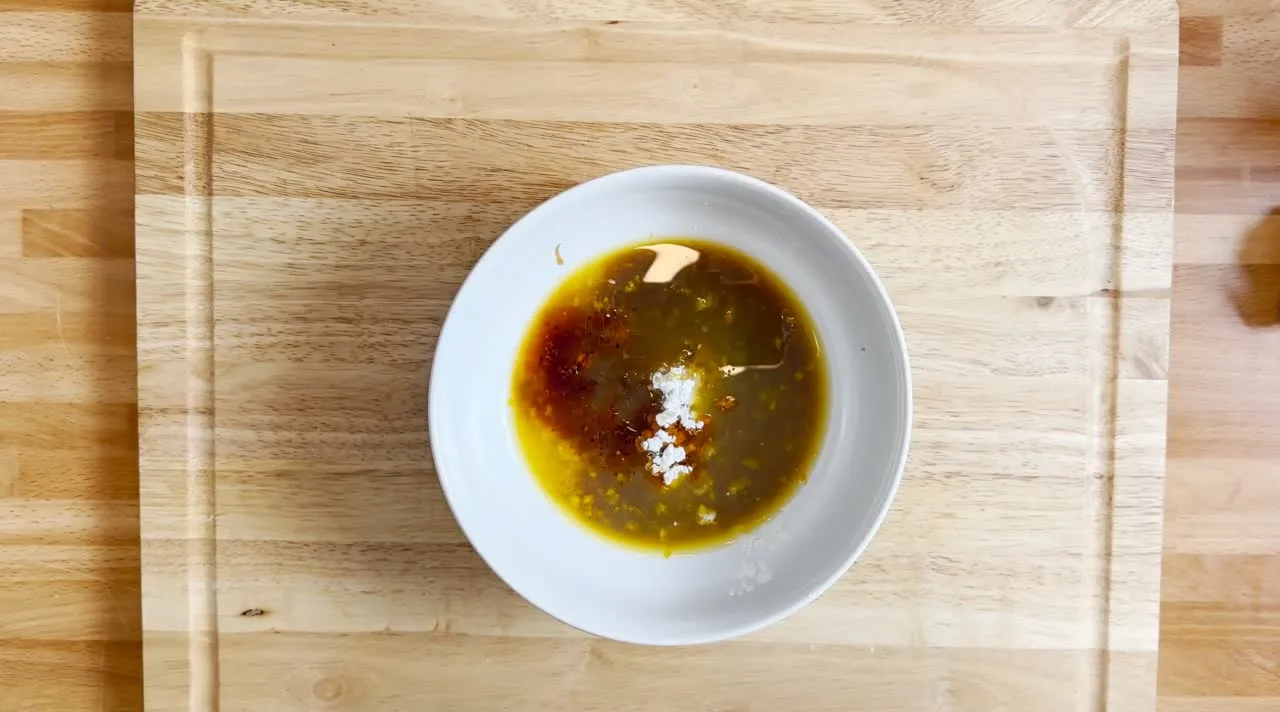 Bowl of mixed sauce with chili oil, soy, and spice on a wooden board, perfect for dipping or seasoning dishes.
