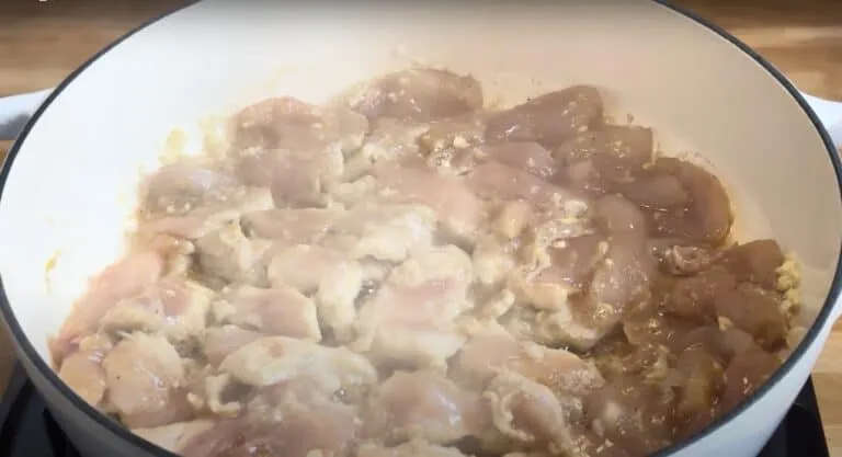 Raw chicken pieces cooking in a white pan, searing for a savory recipe preparation on a stovetop.