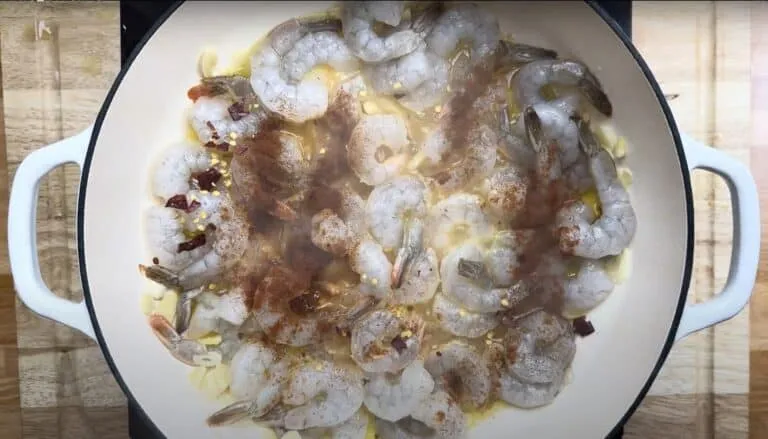 Shrimp cooking in a white pan with garlic and spices on a wooden surface.
