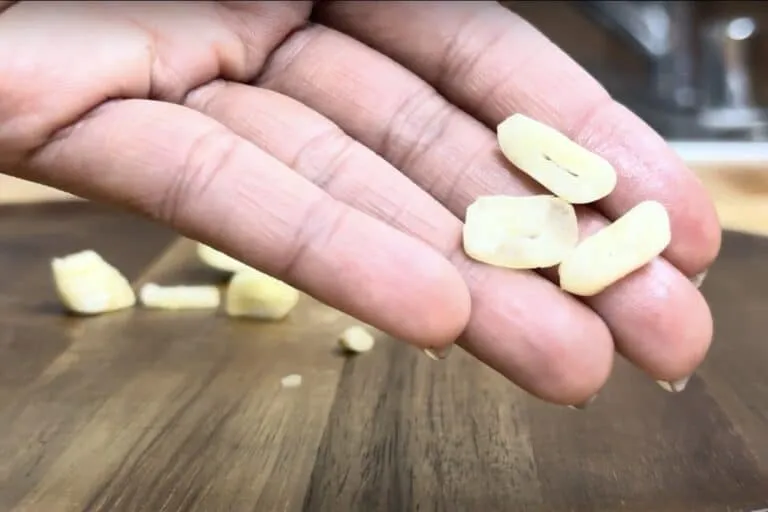Hand holding sliced garlic on a wooden cutting board, ready for cooking.