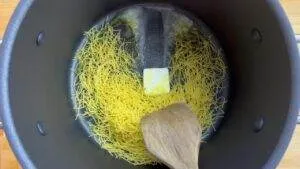 Cooking vermicelli pasta with butter in a pot, stirred with a wooden spoon. Perfect for a quick and easy meal.