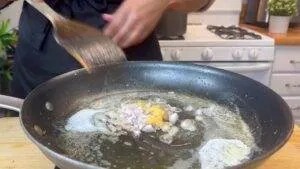 Cooking onions and garlic in a frying pan with butter on a stovetop.