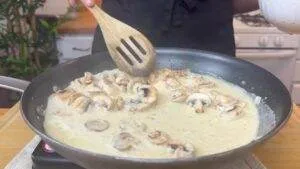 Cooking creamy mushroom sauce in a pan with wooden spatula, perfect for pasta or steak recipes.