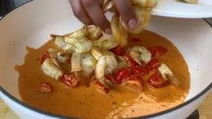 Hand adding shrimp to creamy tomato sauce in pan, creating a delicious seafood dish.