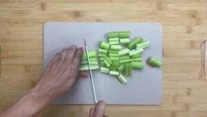 Person chopping fresh celery on a cutting board with a knife.