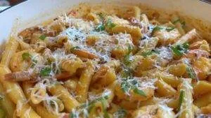 Creamy penne pasta with shrimp, topped with grated cheese and fresh herbs, served in a white bowl.