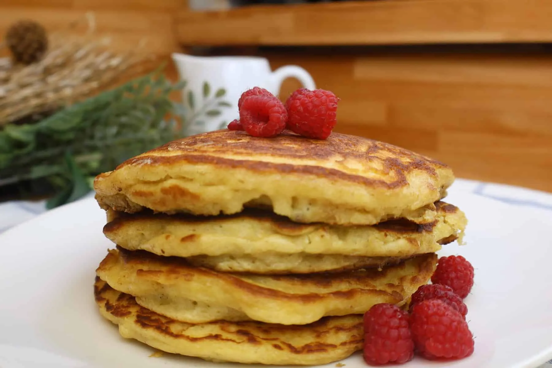 Stack of homemade pancakes topped with fresh raspberries on a white plate.