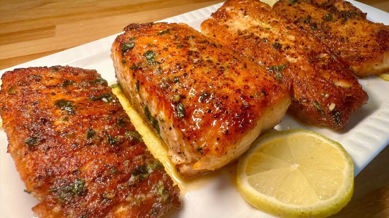 Grilled salmon fillets garnished with herbs and lemon slices on a white plate. Perfect for a healthy, flavorful meal.