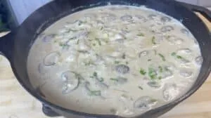 Creamy mushroom sauce in a cast iron skillet, topped with fresh chives. Perfect for pasta or steak dishes.