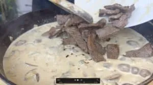 Cooking creamy beef stroganoff with mushrooms in a skillet.