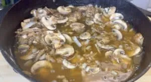 Sautéed mushrooms and onions simmering in a cast iron skillet with savory broth.