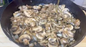 Sautéed mushrooms and onions in a cast iron skillet on a wooden surface, perfect for savory recipes.