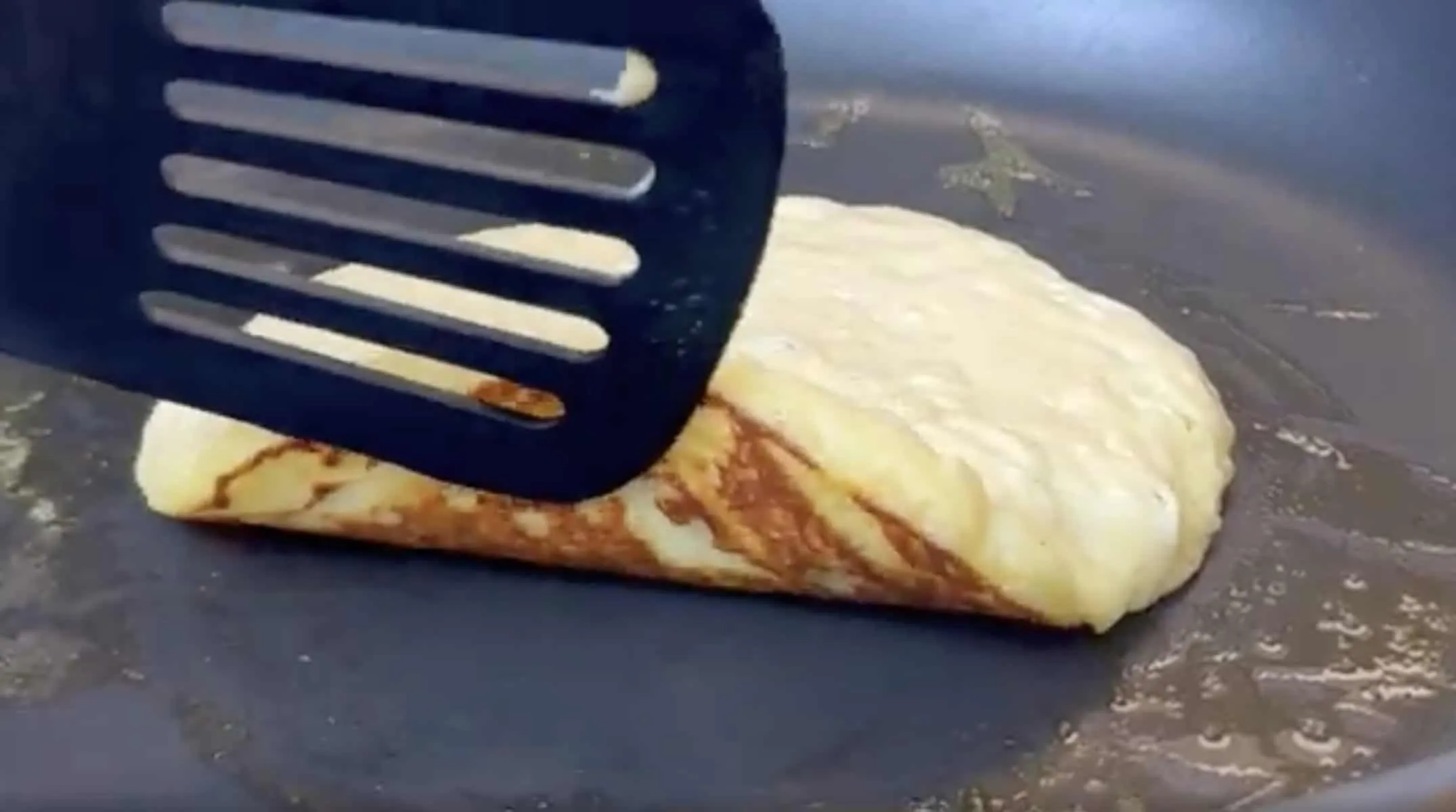 Flipping a pancake in a non-stick pan with a black spatula.