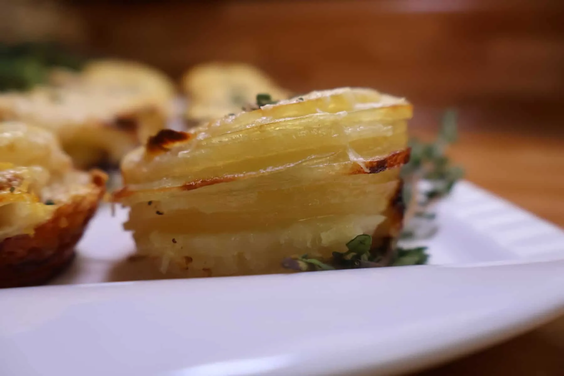Golden potato stacks garnished with herbs on a white plate.