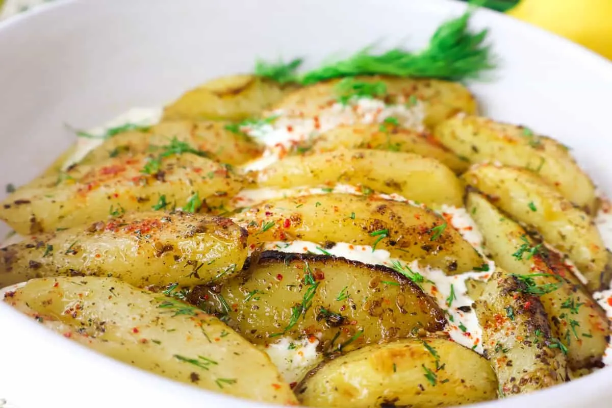 Delicious oven-roasted potatoes with herbs and spices, garnished with fresh dill in a white dish.