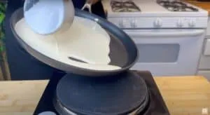Pouring pancake batter into a hot skillet on the stove for perfectly fluffy homemade pancakes.