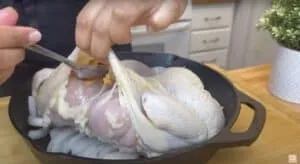 Adding seasoning under chicken skin in a skillet for roasting.