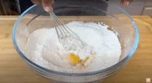 Mixing eggs and flour in a glass bowl with a whisk on a wooden surface. Perfect for baking recipes.