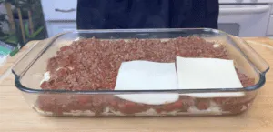 Glass dish with layered meat sauce and cheese, ready for baking. Delicious homemade lasagna preparation.