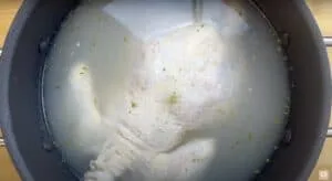 Chicken leg simmering in seasoned water inside a large black pot.