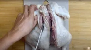 Person cutting a whole chicken on a board, preparing it for cooking.