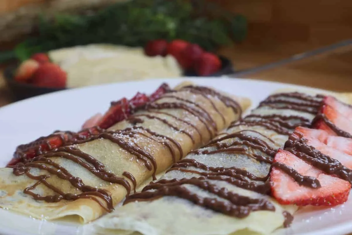 Delicious crepes topped with chocolate drizzle and fresh strawberries on a white plate.