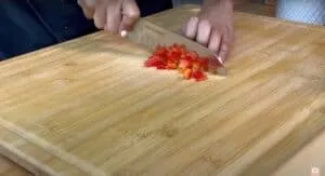 Person dicing red bell pepper on a wooden cutting board with a knife.