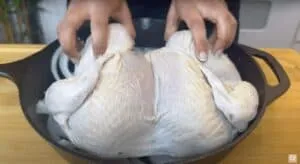 Raw chicken being prepared in a cast iron skillet with onions, ready for roasting.