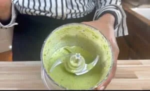 Person holding a blender cup with fresh green smoothie in a kitchen setting.