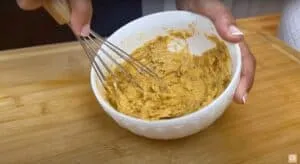 Mixing spicy butter chicken marinade in a white bowl with a whisk on a wooden board.