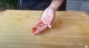 Hand holding grape tomato and seed on cutting board. Fresh ingredients displayed for cooking or salad preparation.