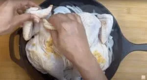 Person preparing seasoned chicken in a skillet over sliced onions for cooking.