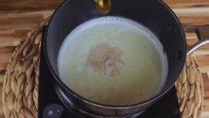 Pot of simmering milk on a stove, with a drop of oil being added for cooking.