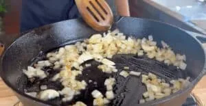 Sautéing chopped onions and garlic in a cast iron skillet, cooking in progress with a wooden spatula.