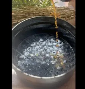 Fresh blueberries in a pot with honey drizzle, sunlight shining on rustic wooden table. Perfect for healthy recipes.
