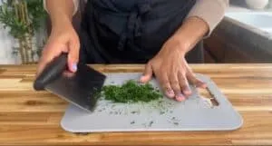 Person chopping fresh herbs on a cutting board in a kitchen setting.