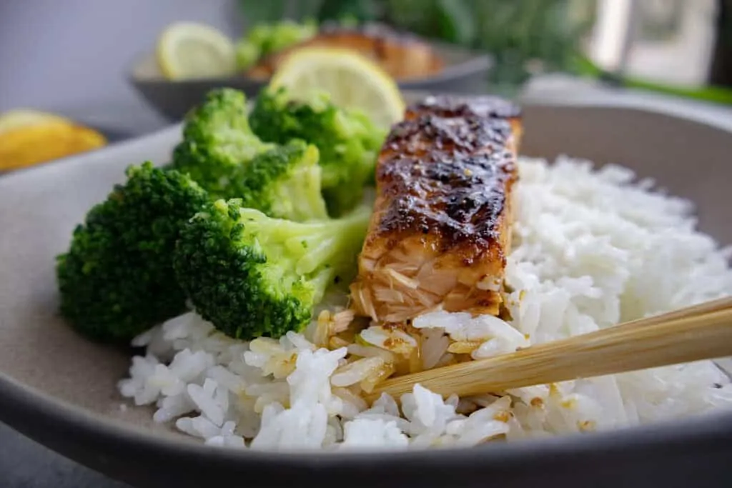 Grilled honey orange salmon with broccoli and rice, garnished with lemon, in a ceramic bowl, close-up.